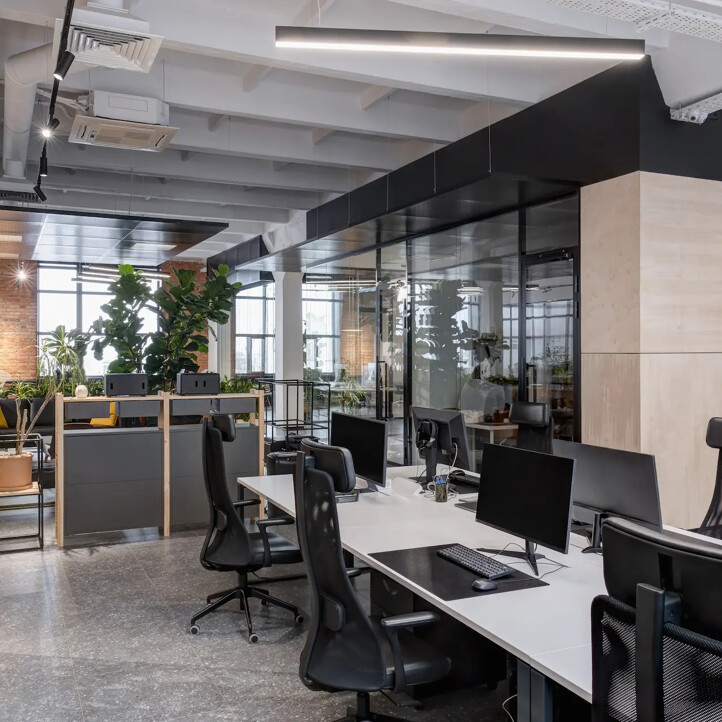 Offenes Büro mit Schreibtischen, Computern und grünen Pflanzen.