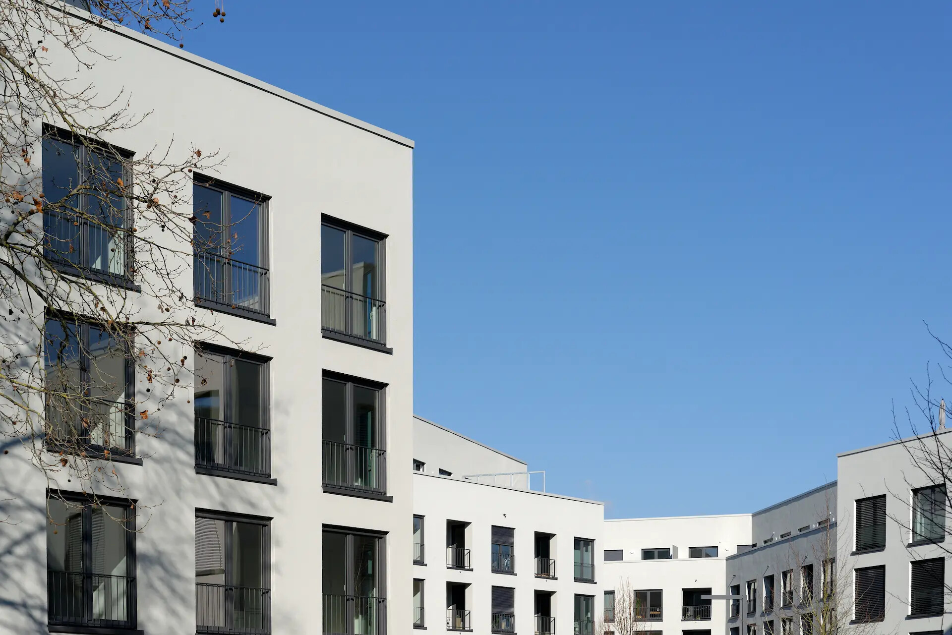 Weißes Wohngebäude mit großen Fenstern vor blauem Himmel.