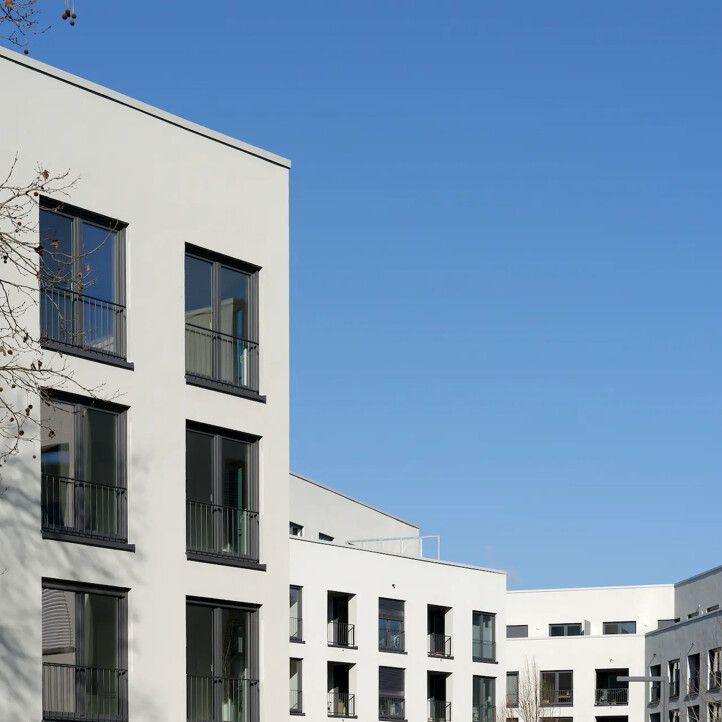 Weißes Wohngebäude mit großen Fenstern vor blauem Himmel.