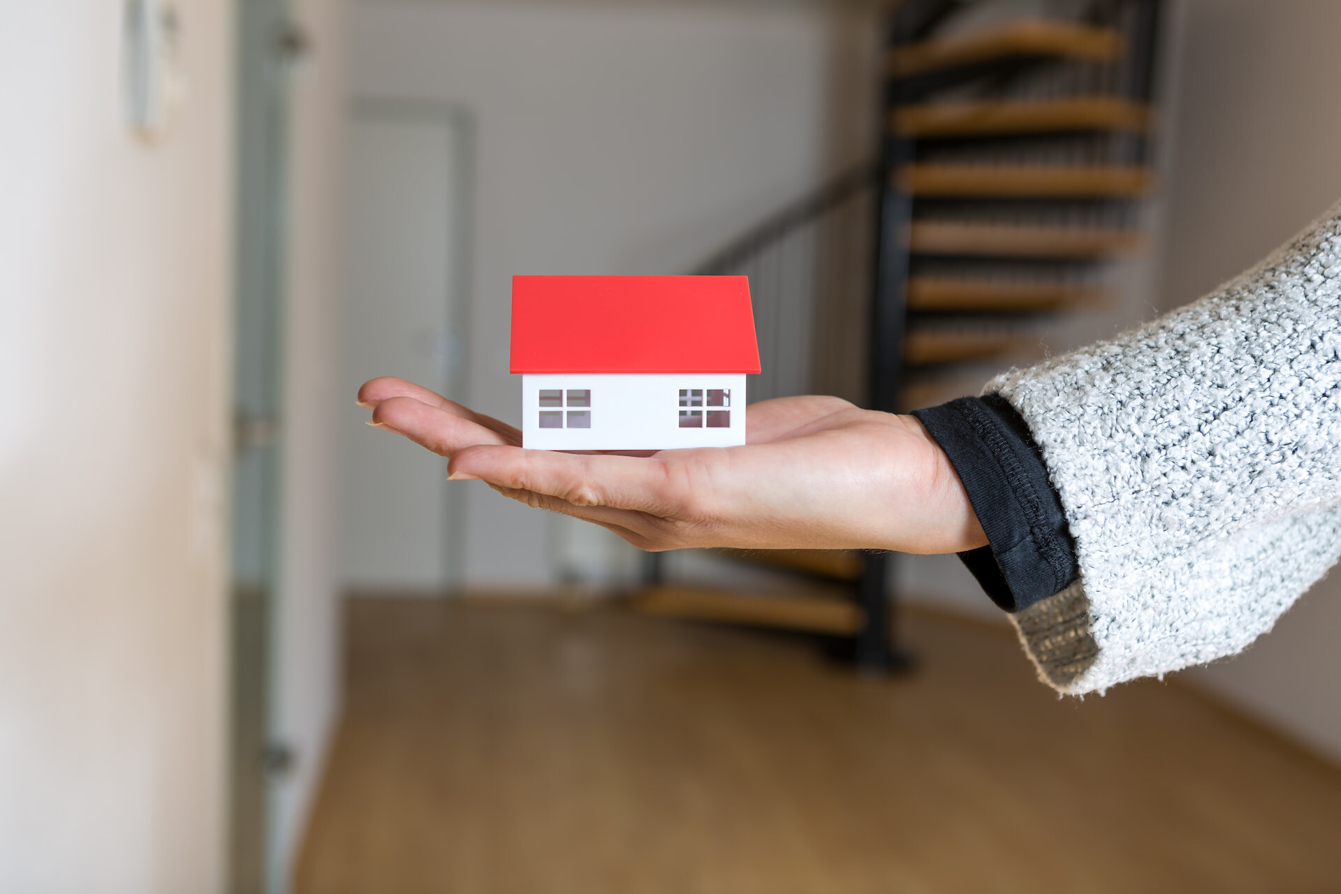 Hand hält Miniaturhaus mit rotem Dach in modernem Zuhause.