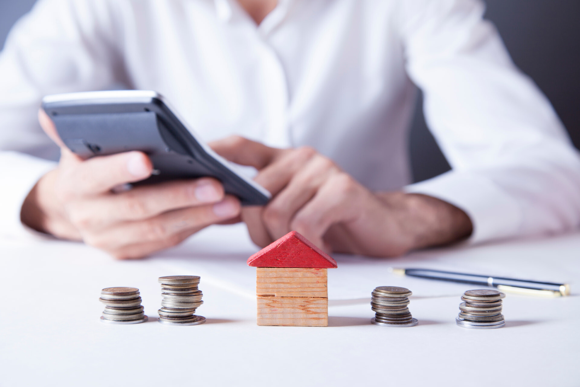 Taschenrechner, Holzhaus und Münzen für die Finanzplanung.