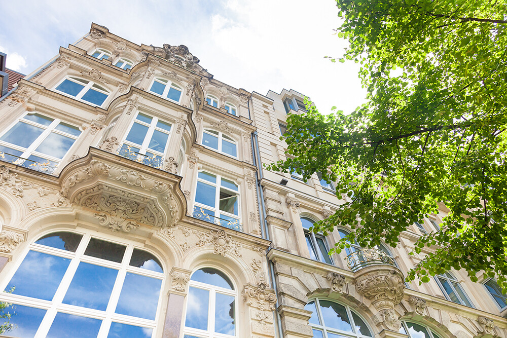 Historisches Gebäude mit Balkonen, großem Fenster, neben Baum.