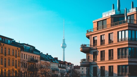 Berliner Fernsehturm hinter modernem und historischem Gebäude, blauer Himmel.
