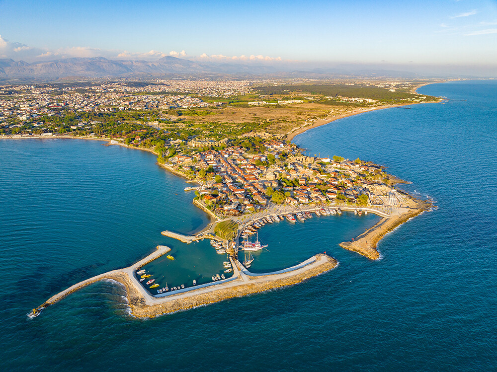 Küstenstadt mit Hafen, Wellenbrechern und blauem Meer von oben.