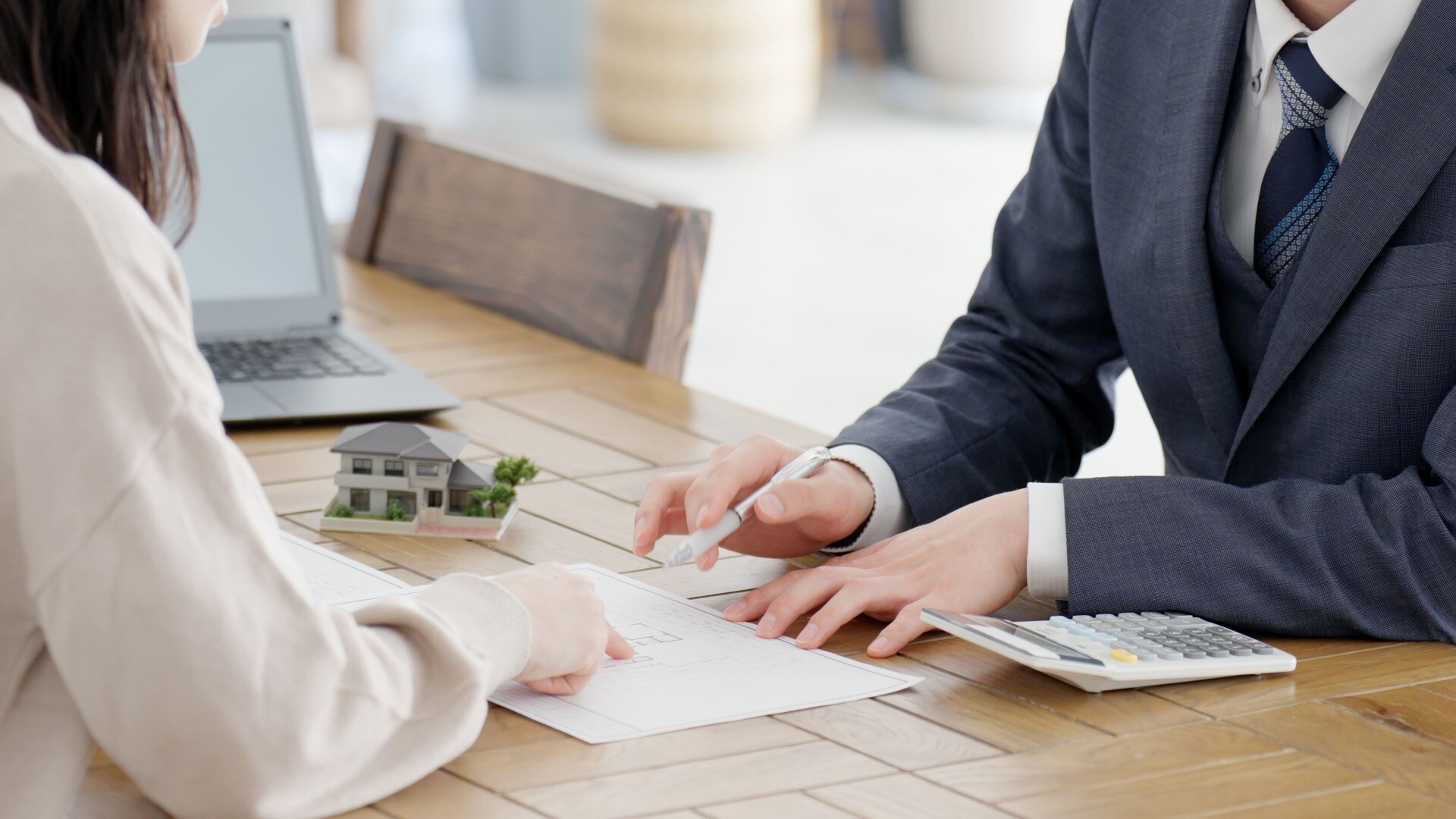 Zwei Personen prüfen Unterlagen am Schreibtisch mit Laptop.