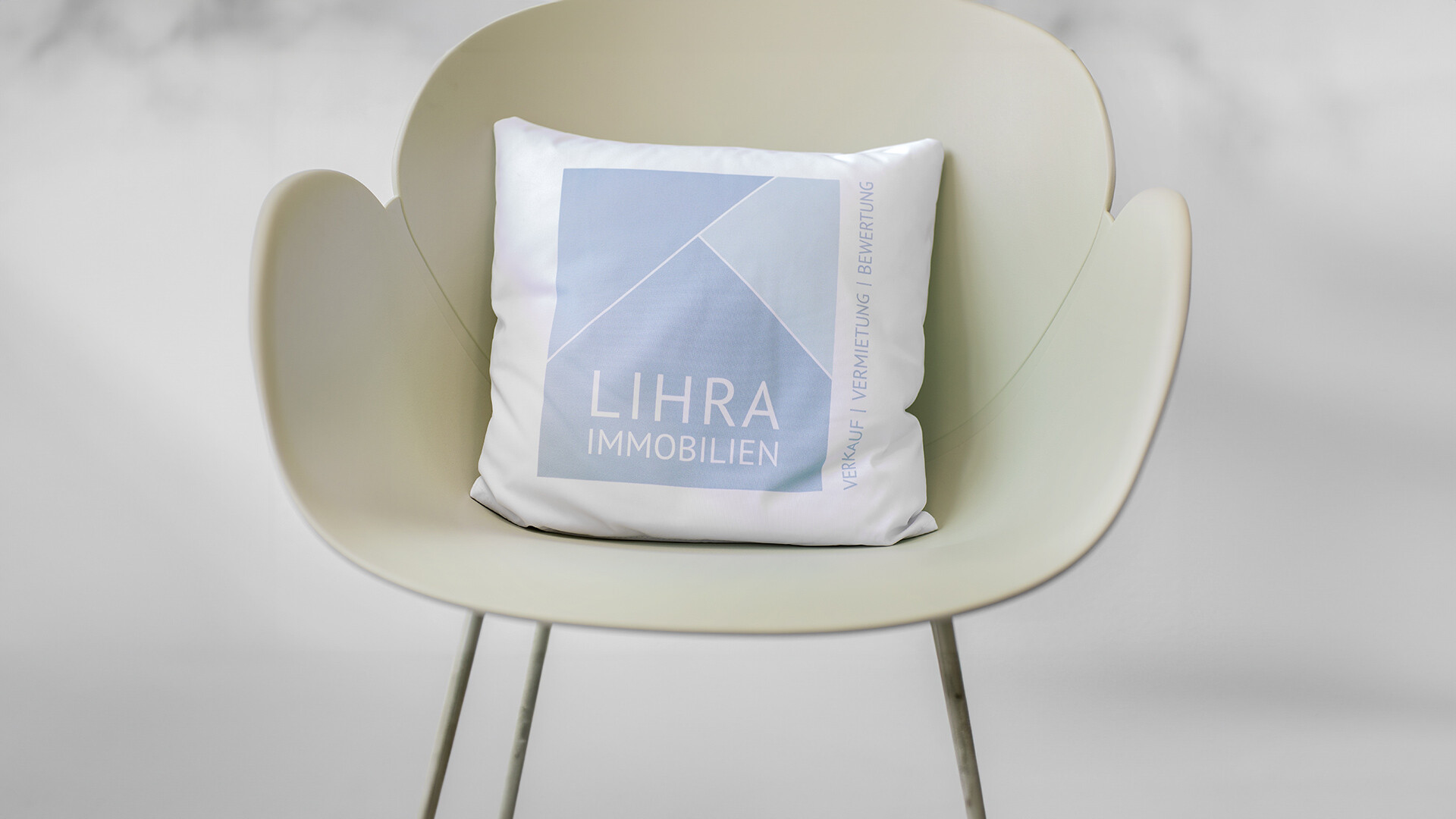 Weißer Stuhl, Kissen mit LIHRA IMMOBILIEN-Logo (deutscher Text).