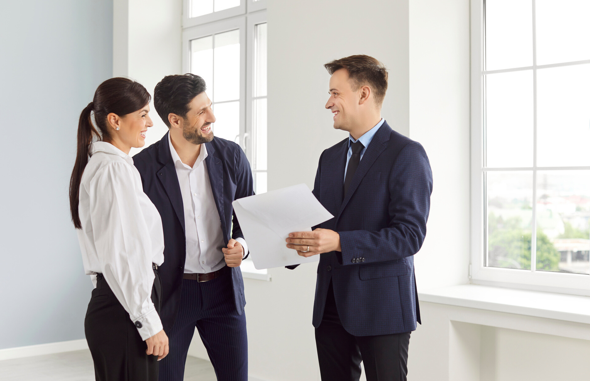 Makler spricht mit einem jungen Paar in leerer Wohnung