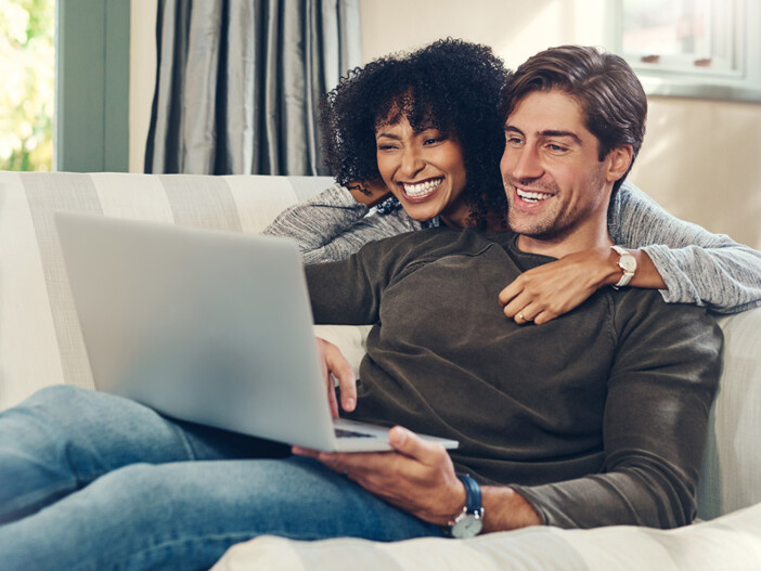 Mann und Frau sitzen auf der Couch und suchen mit dem Laptop nach Immobilien