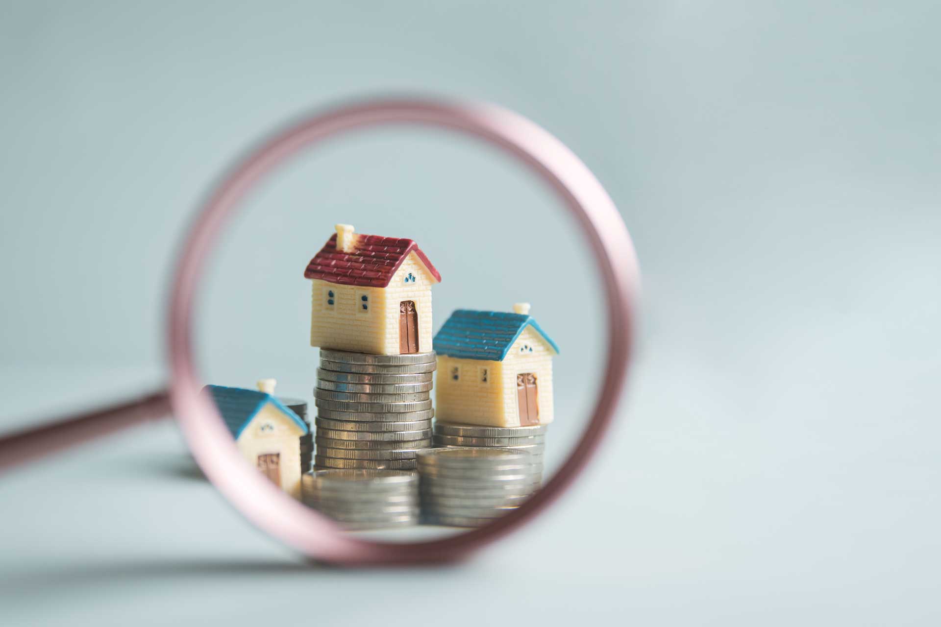 Lupe zeigt auf Modellhäuser auf Münzstapeln: Symbol für Wert der Immobilie nach Zustand