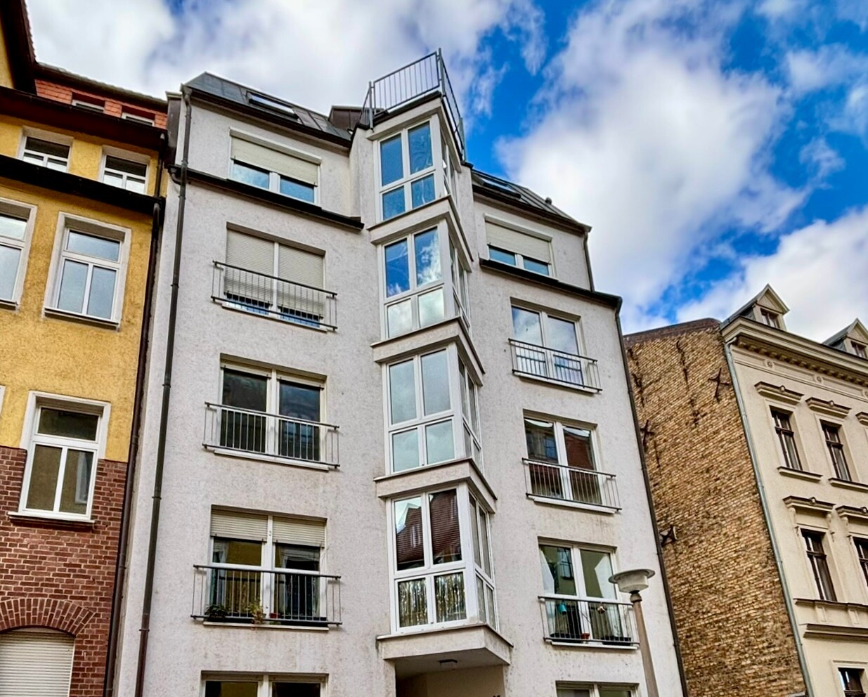 Modernes weißes Haus mit Glasbalkonen zwischen Altbauten.