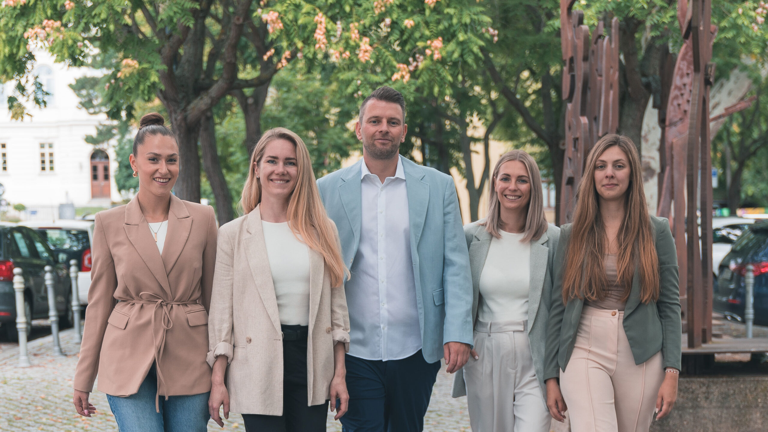 Das 5-köpfige Team von living halle draußen, lächelnd, vor Bäumen und geparkten Autos.