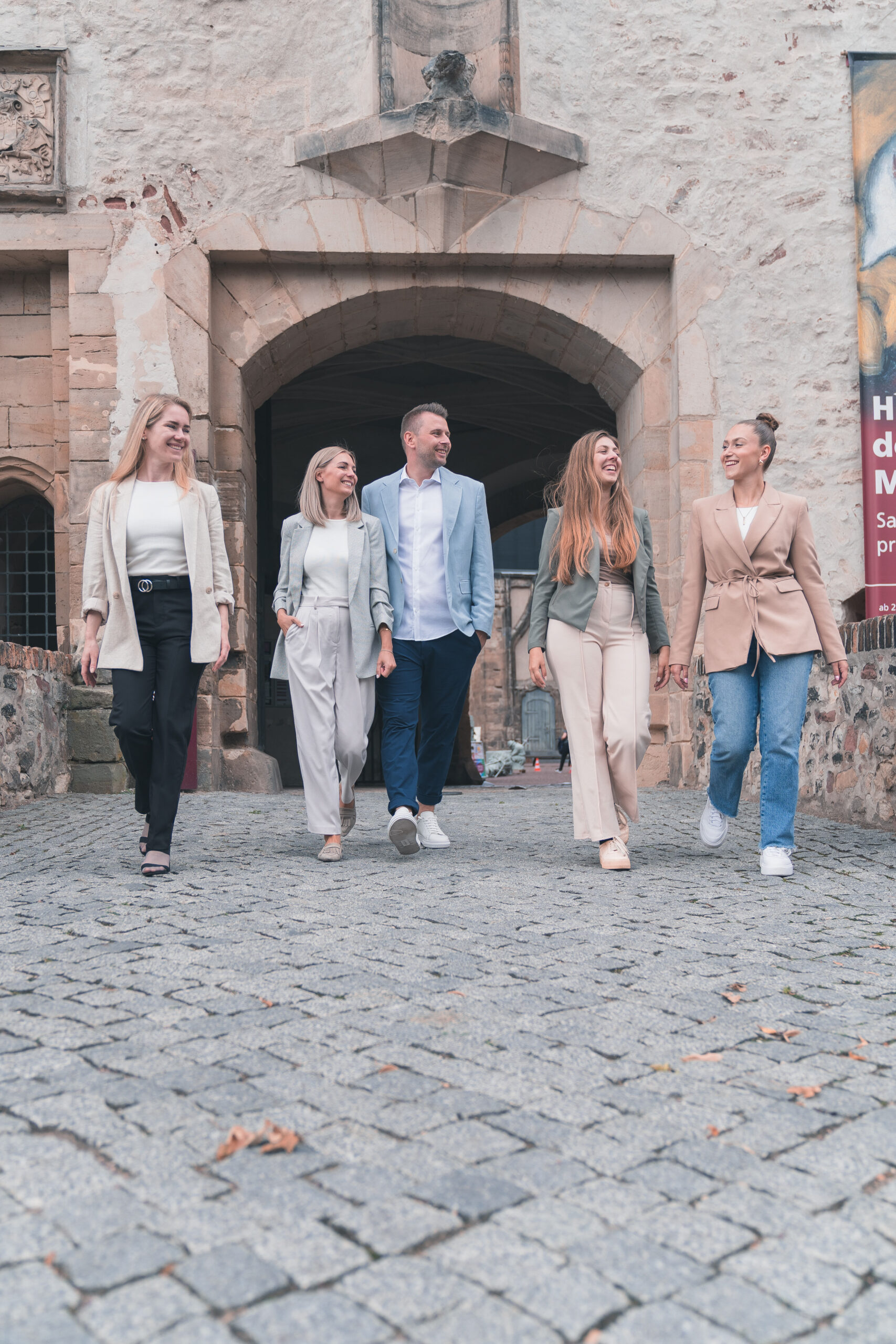 Das 5-köpfige Team von living halle steht lächelnd vor einem steinernen Gebäude.