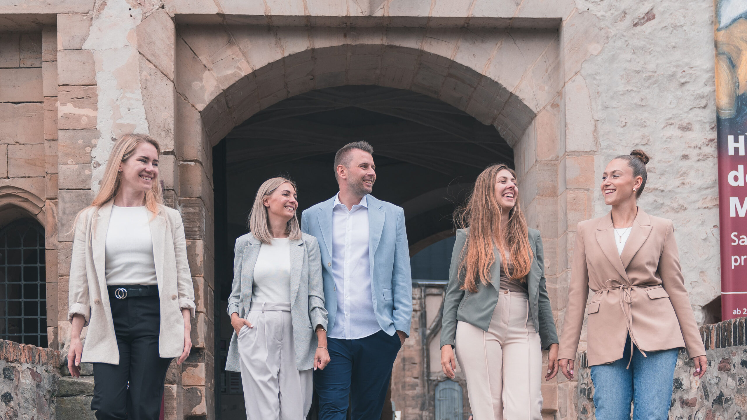 Das 5-köpfige Team von living halle steht lächelnd vor einem steinernen Gebäude.