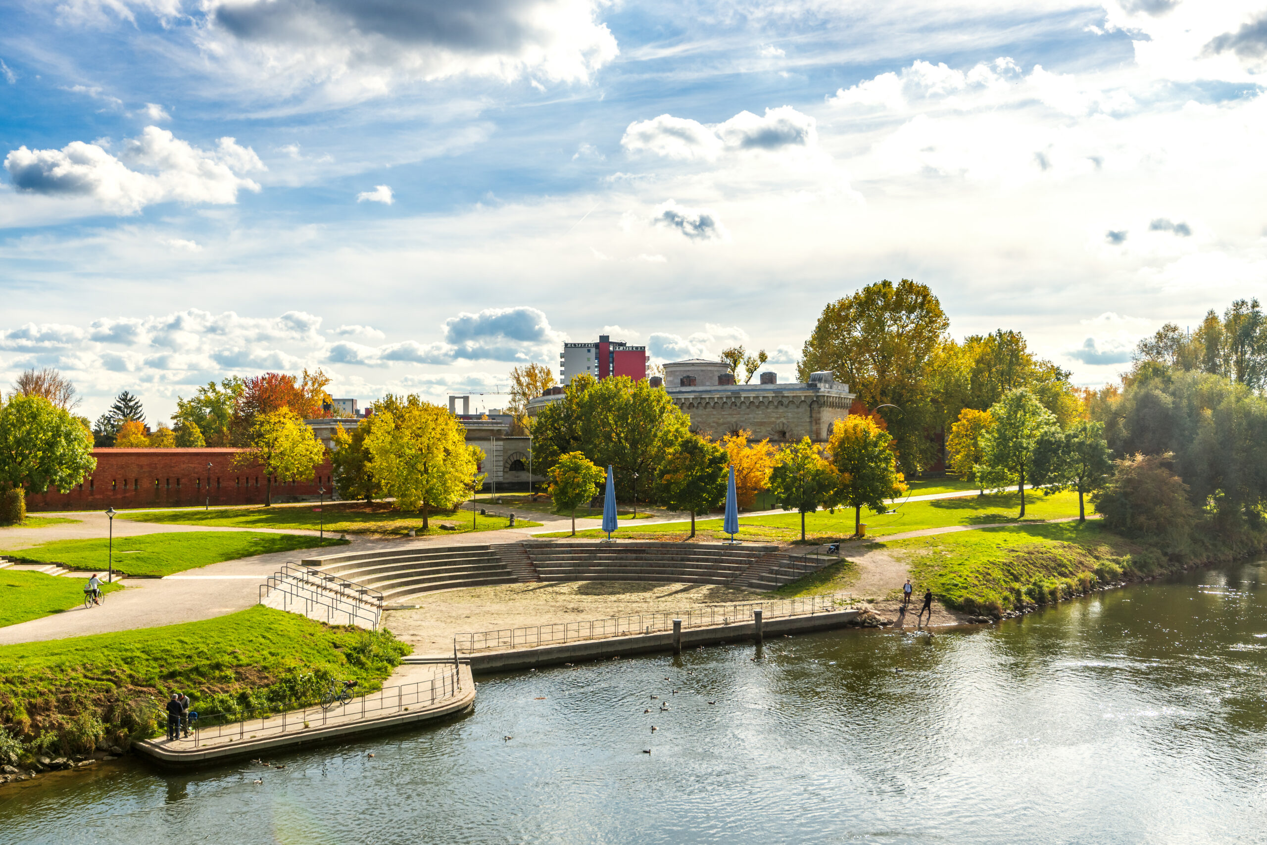 Amphitheater am Fluss, umgeben von Herbstbäumen und Wolken.