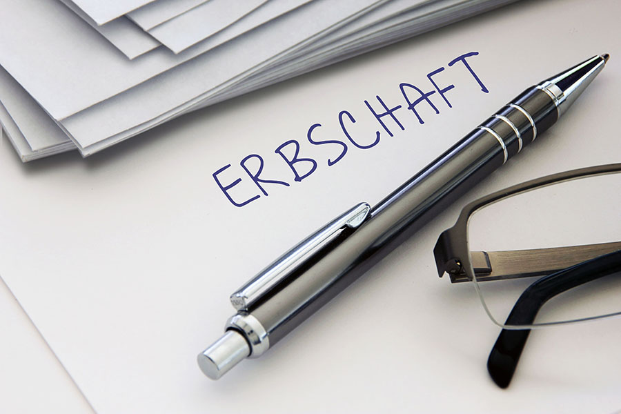 Stift, Brille, Papiere und "ERBSCHAFT" auf einem Blatt.