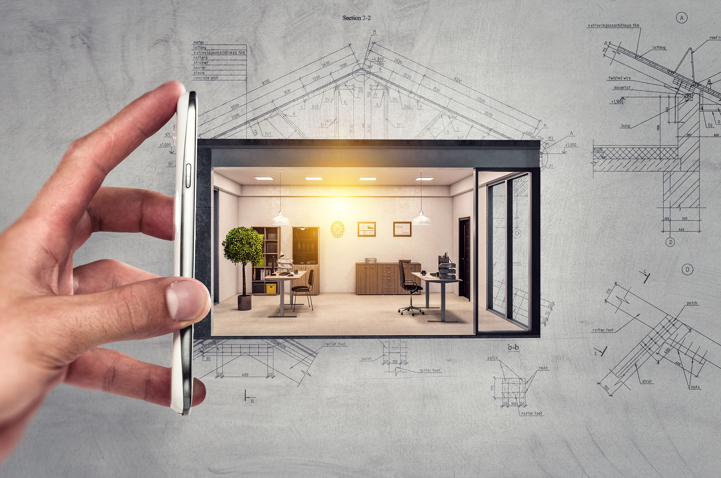 Hand mit Handy vor Büro und Architektenplänen im Hintergrund.