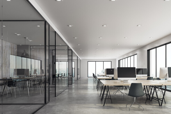 Helles Großraumbüro mit Glaswänden, Schreibtischen und PCs.