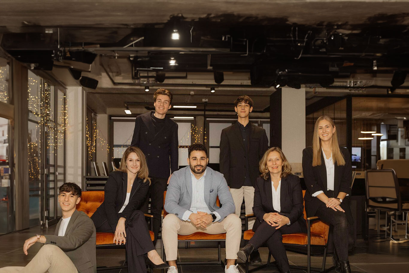 Sieben Personen sitzen in moderner Büroeinrichtung auf orangen Stühlen.