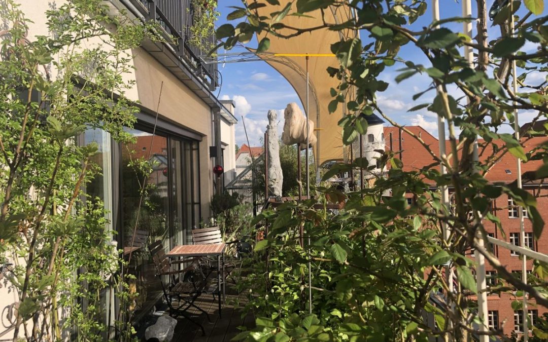 Balkon mit Pflanzen, Möbeln und Blick auf rote Dächer.