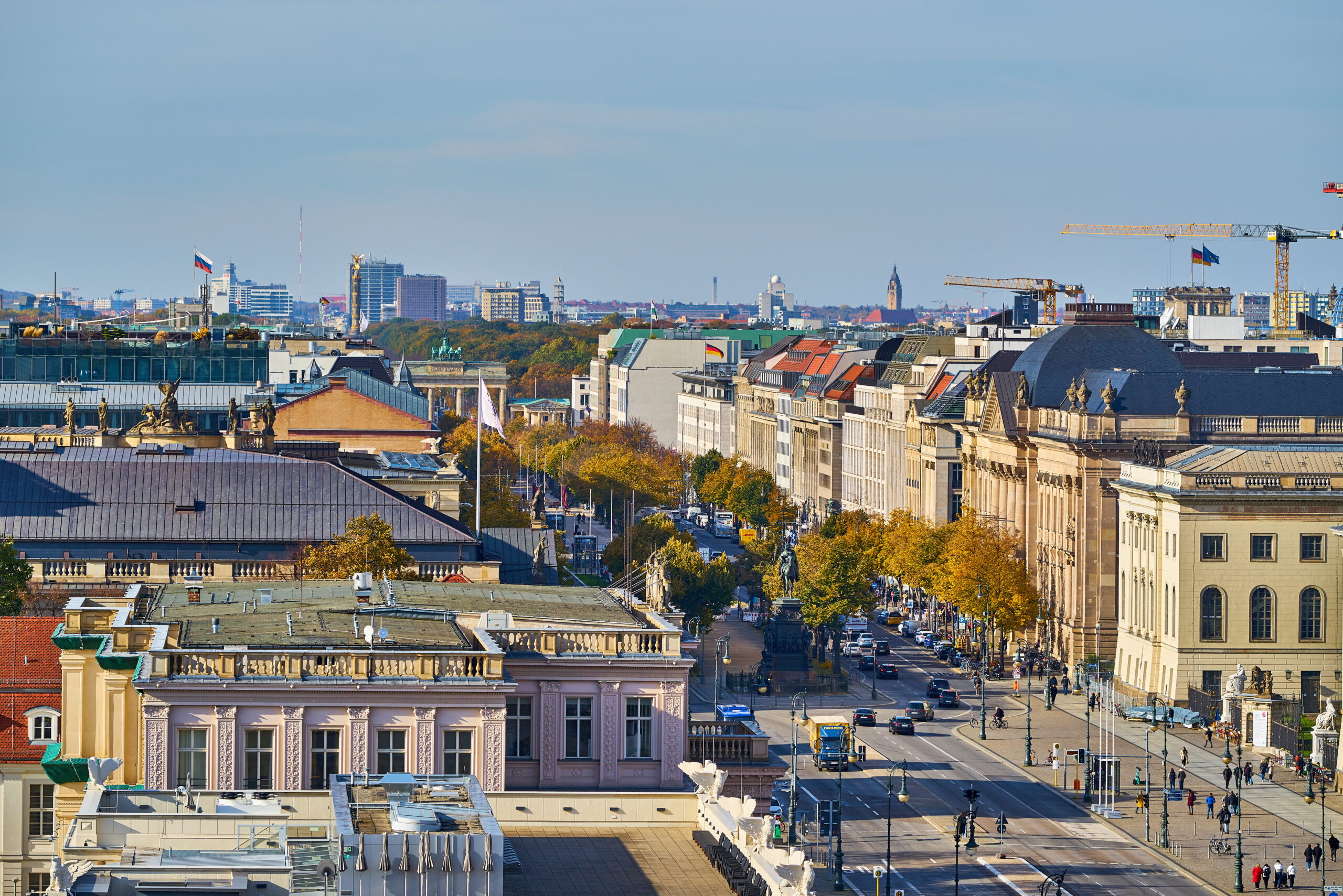 Belebte Straße mit historischen Gebäuden und Bäumen bei klarem Wetter.