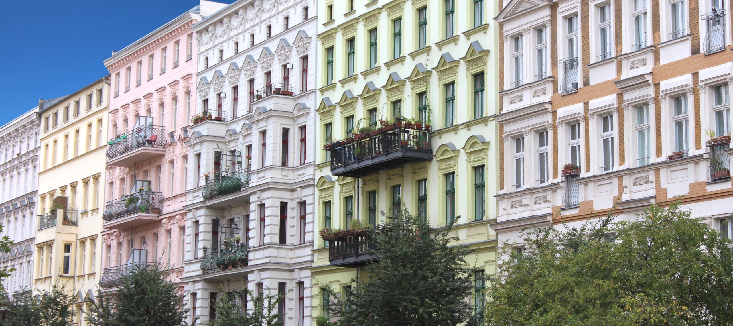 Bunte Altbauten mit Balkonen und Bäumen vor blauem Himmel, Mehrfamilienhäuser zur Vermietung