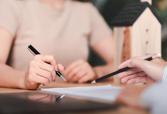 Zwei Personen besprechen Dokumente neben einem Holzhaus-Modell.
