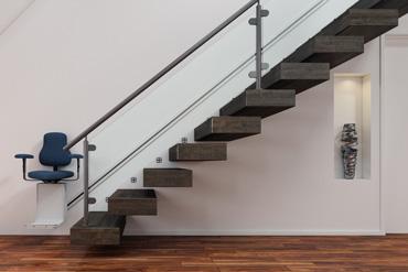 Holztreppe mit Treppenlift links an weißer Wand und Holzboden.