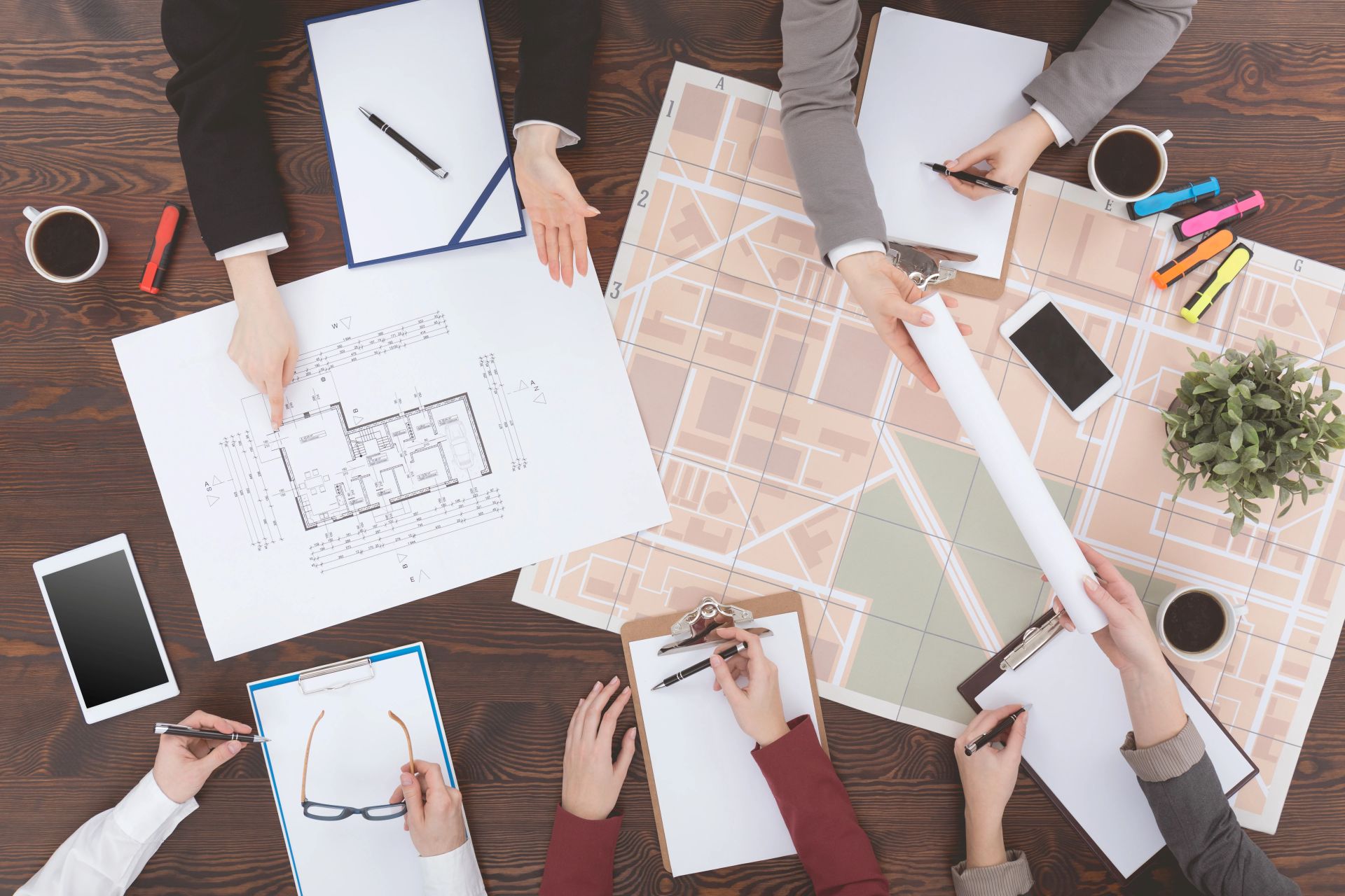 Menschen prüfen Blaupausen und Karten an einem Tisch mit Bürobedarf.