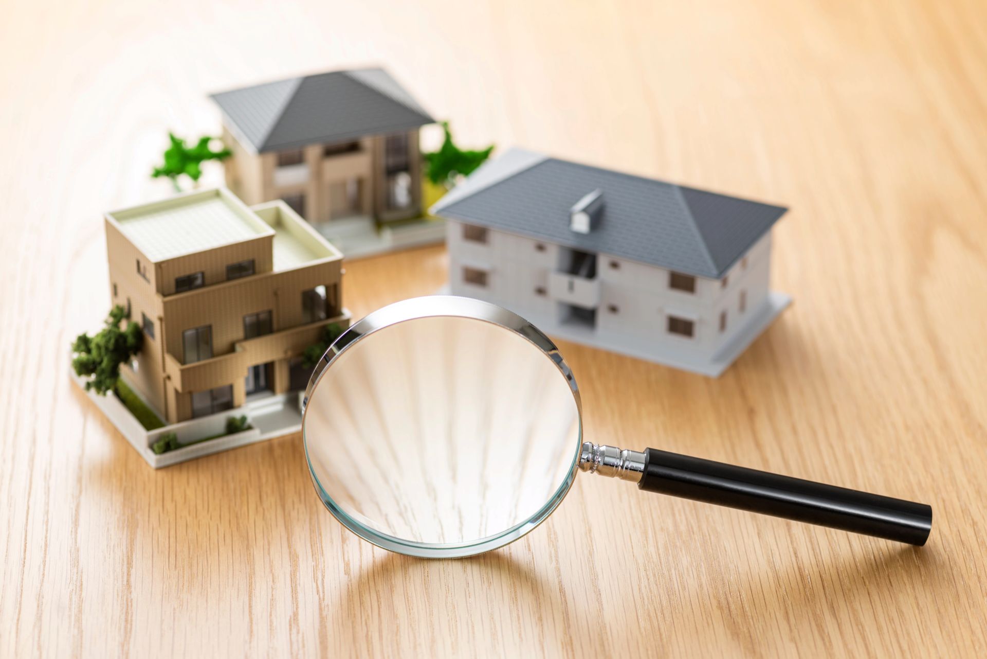 Lupe neben zwei Modellhäusern auf Holzoberfläche.