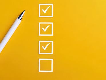 Eine Checkliste vor einem gelben Hintergrund, daneben ein Stift