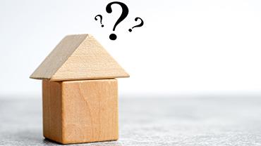 Ein Hausmodell aus Bauklötzen mit Fragenzeichen