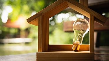 Eine Glühbirne steht in einem Hausmodell aus Holz