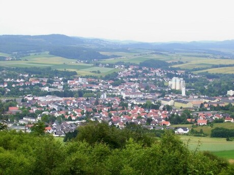 Kleinstadt mit roten Dächern, grünen Feldern, hügeliger Landschaft.