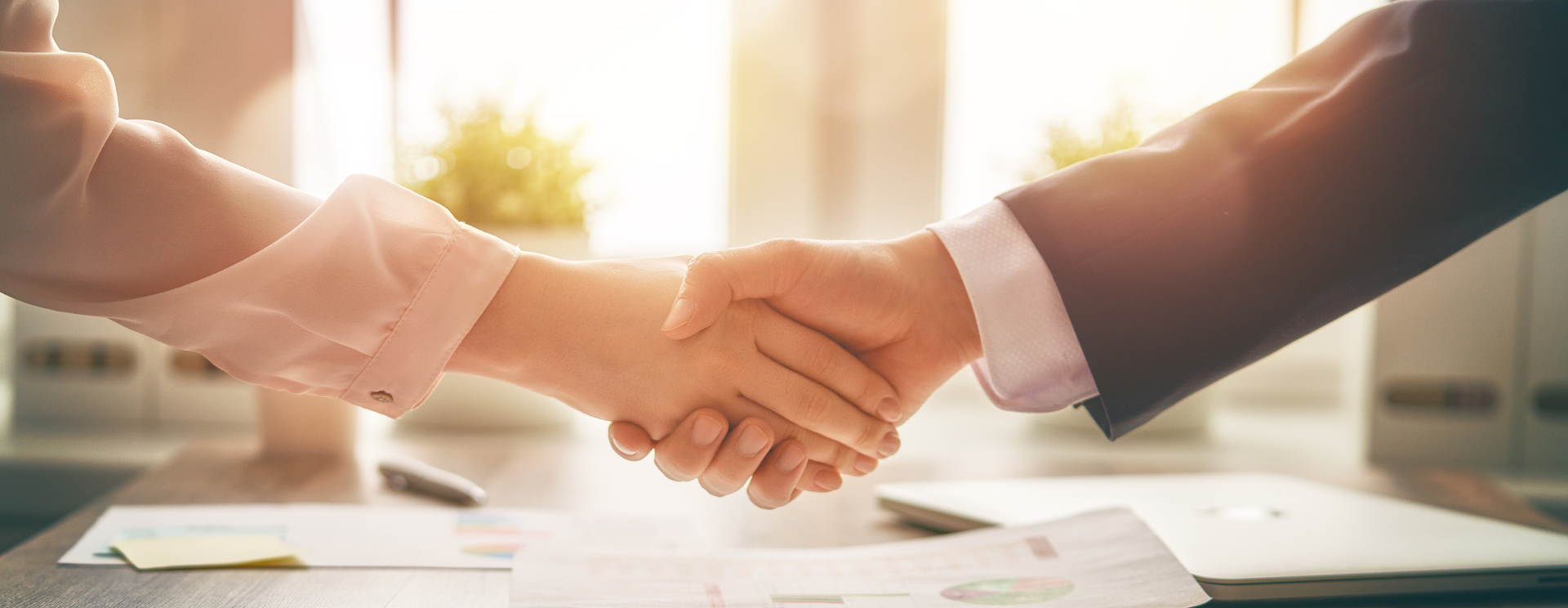 Zwei Personen in Geschäftskleidung schütteln sich in einem Büro die Hände.