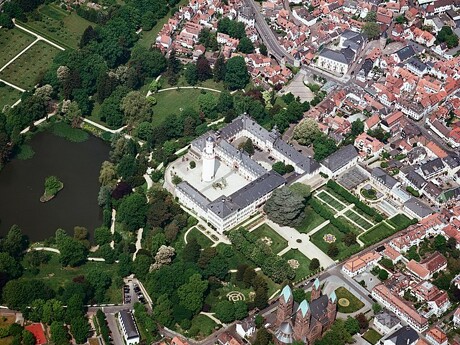 Luftbild eines großen Schlosses mit Gärten und umliegender Stadt.