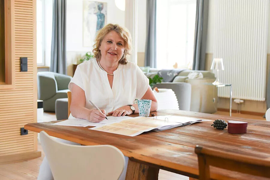 Frau schreibt am Tisch und lächelt, Tasse daneben.