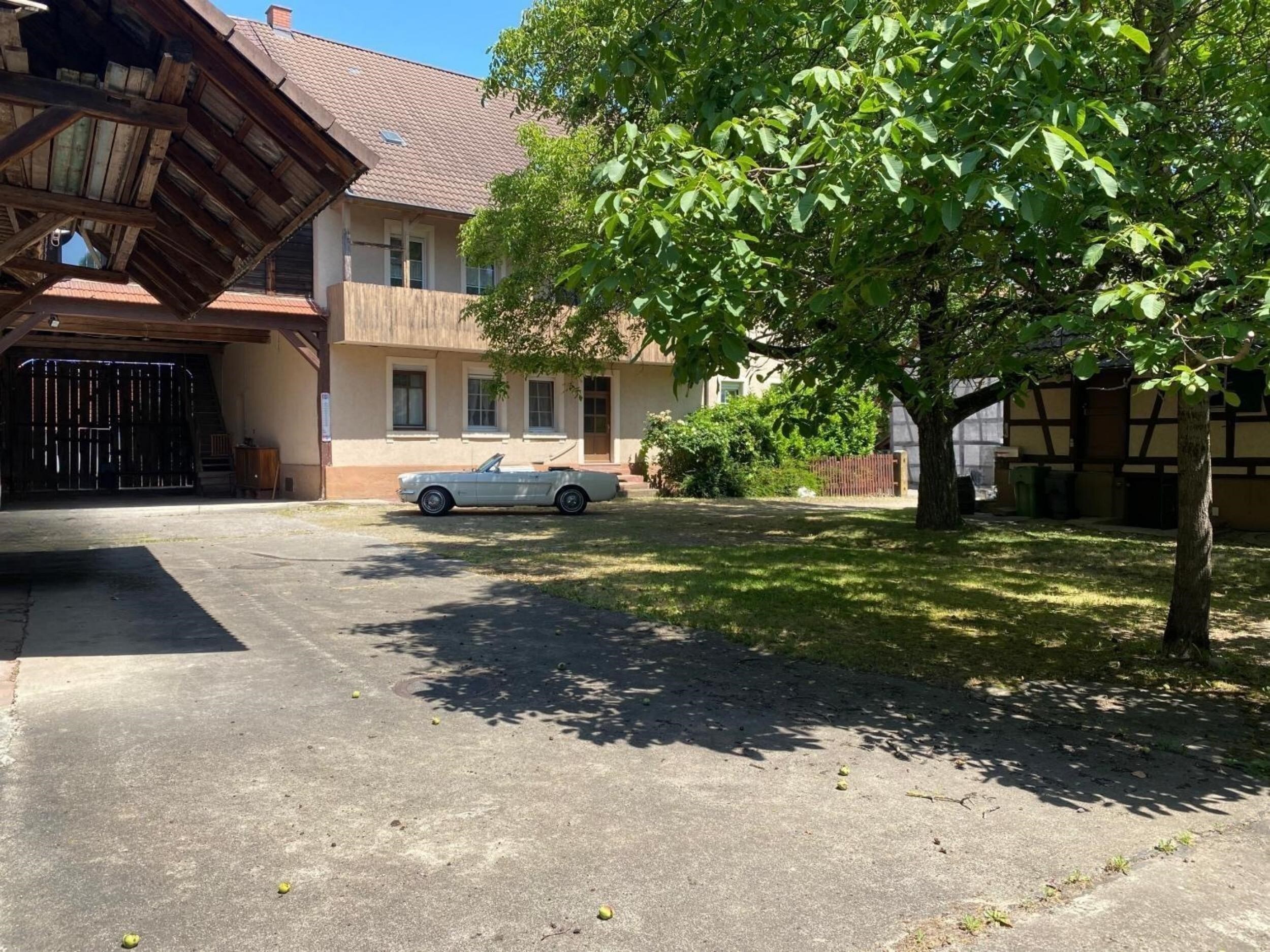 Weißes Cabrio im sonnigen Innenhof zwischen Baum und beigem Haus.
