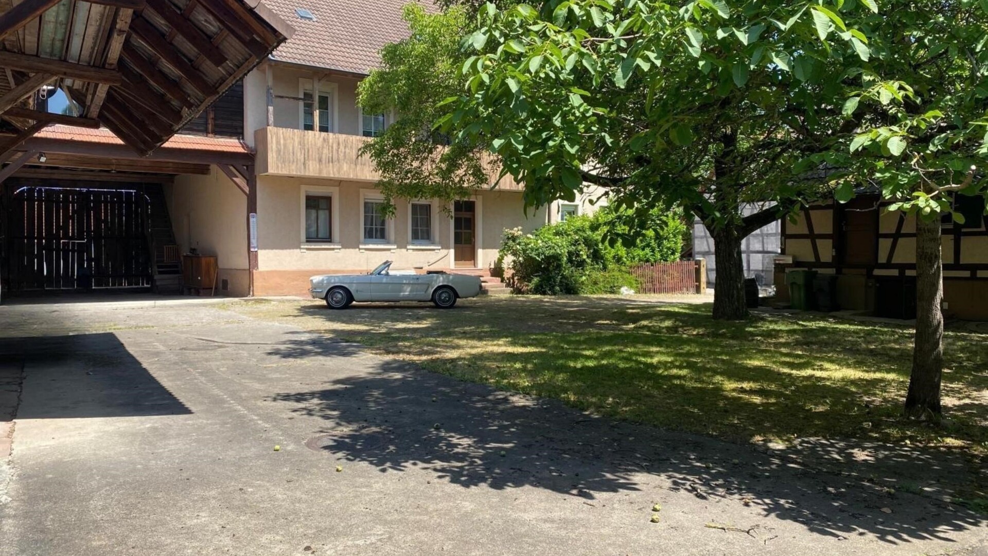 Weißes Cabrio im sonnigen Innenhof zwischen Baum und beigem Haus.