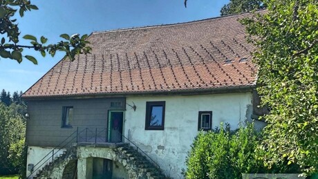 Altes Bauernhaus mit Steinstufen und grünem Gras drumherum.