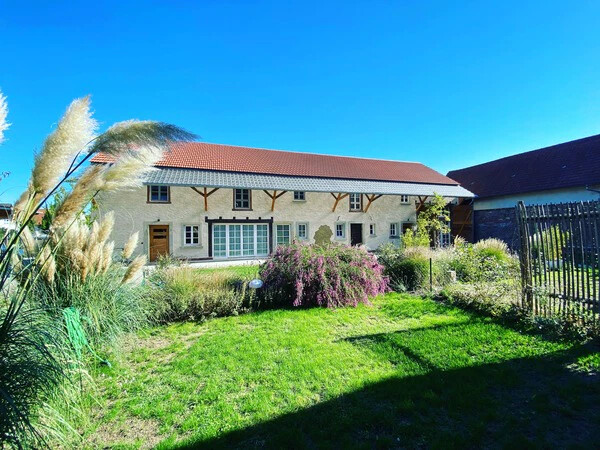 Rustikales Haus mit rotem Dach, grünem Garten und hohen Gräsern.