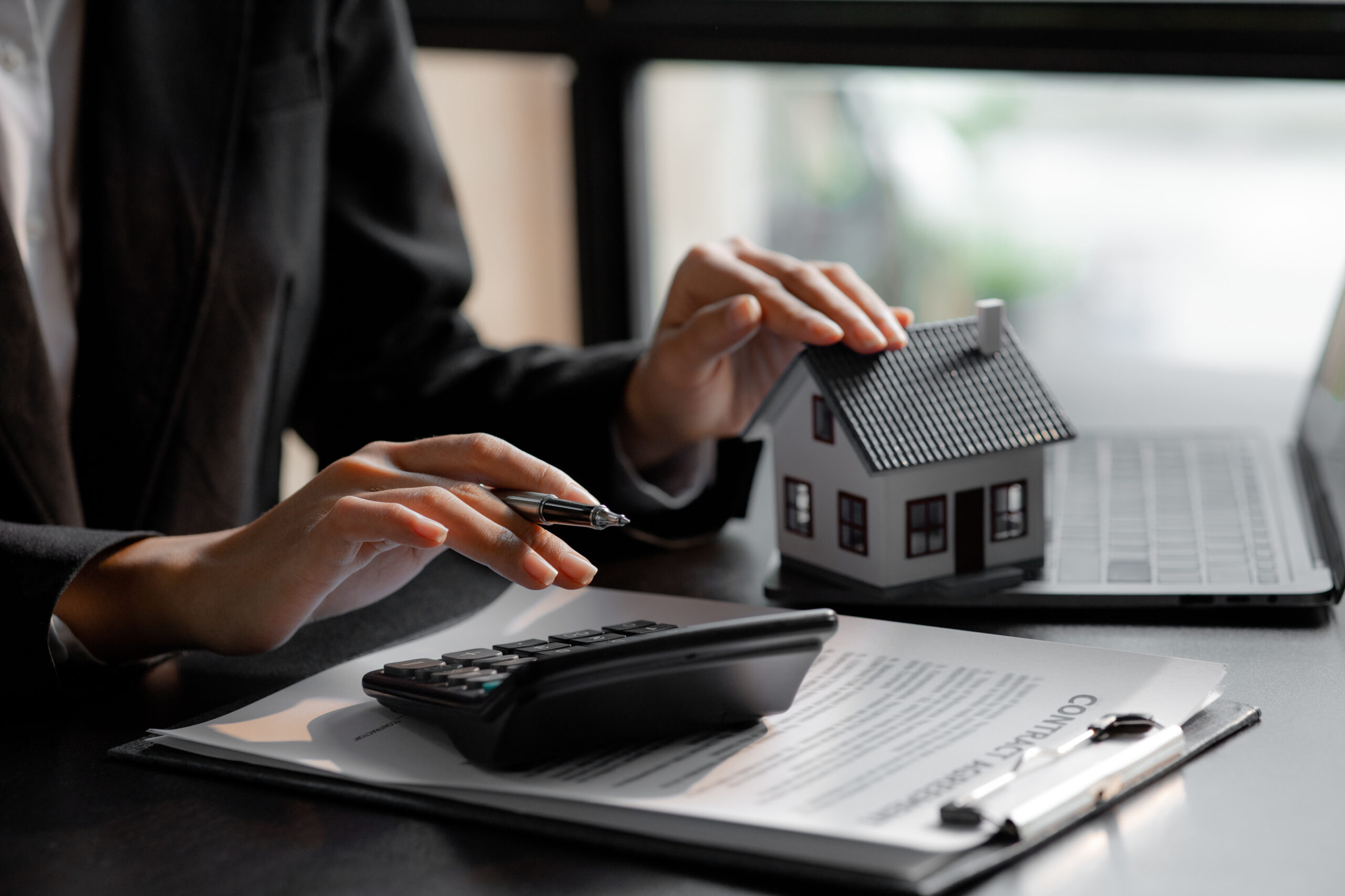 Frau hält Modellhaus und nutzt Taschenrechner