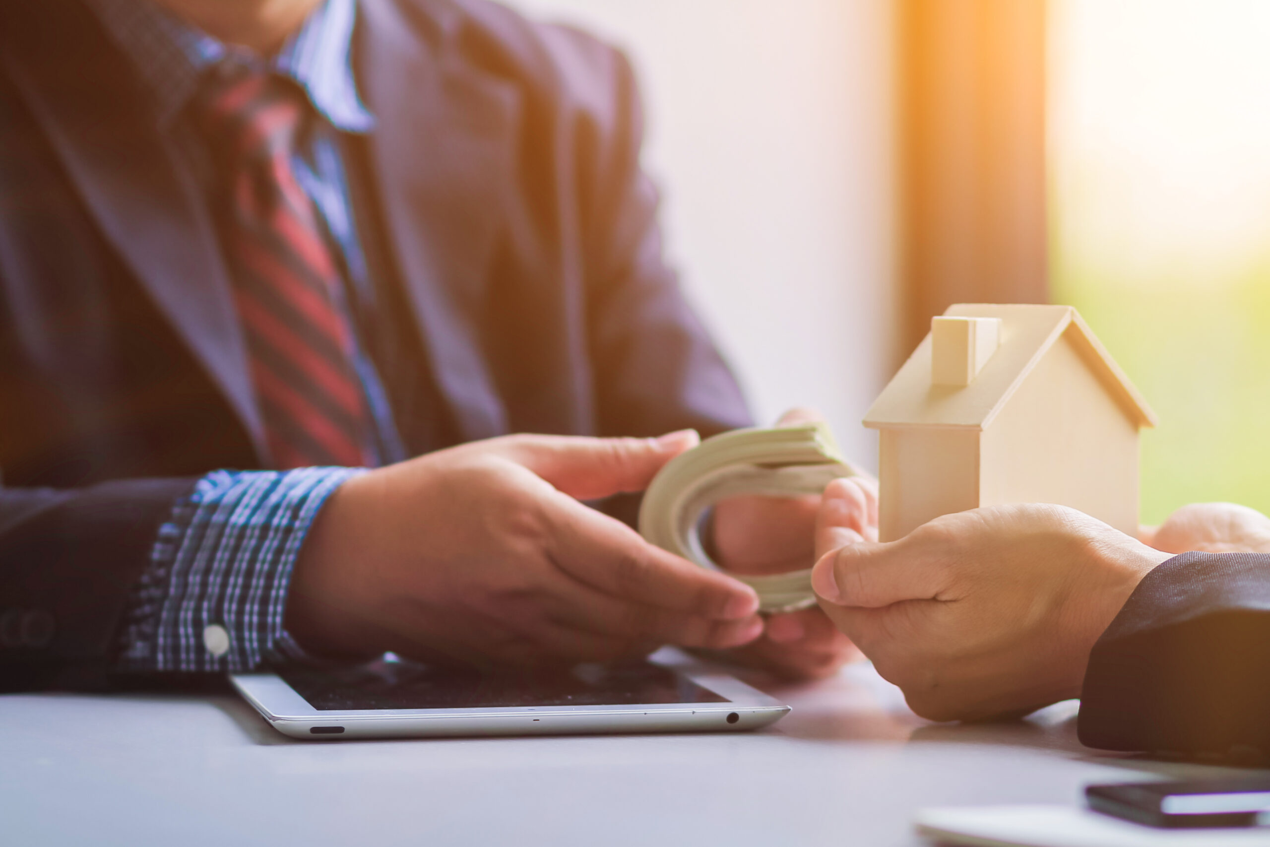 Hände halten Modellhaus und Geldscheine