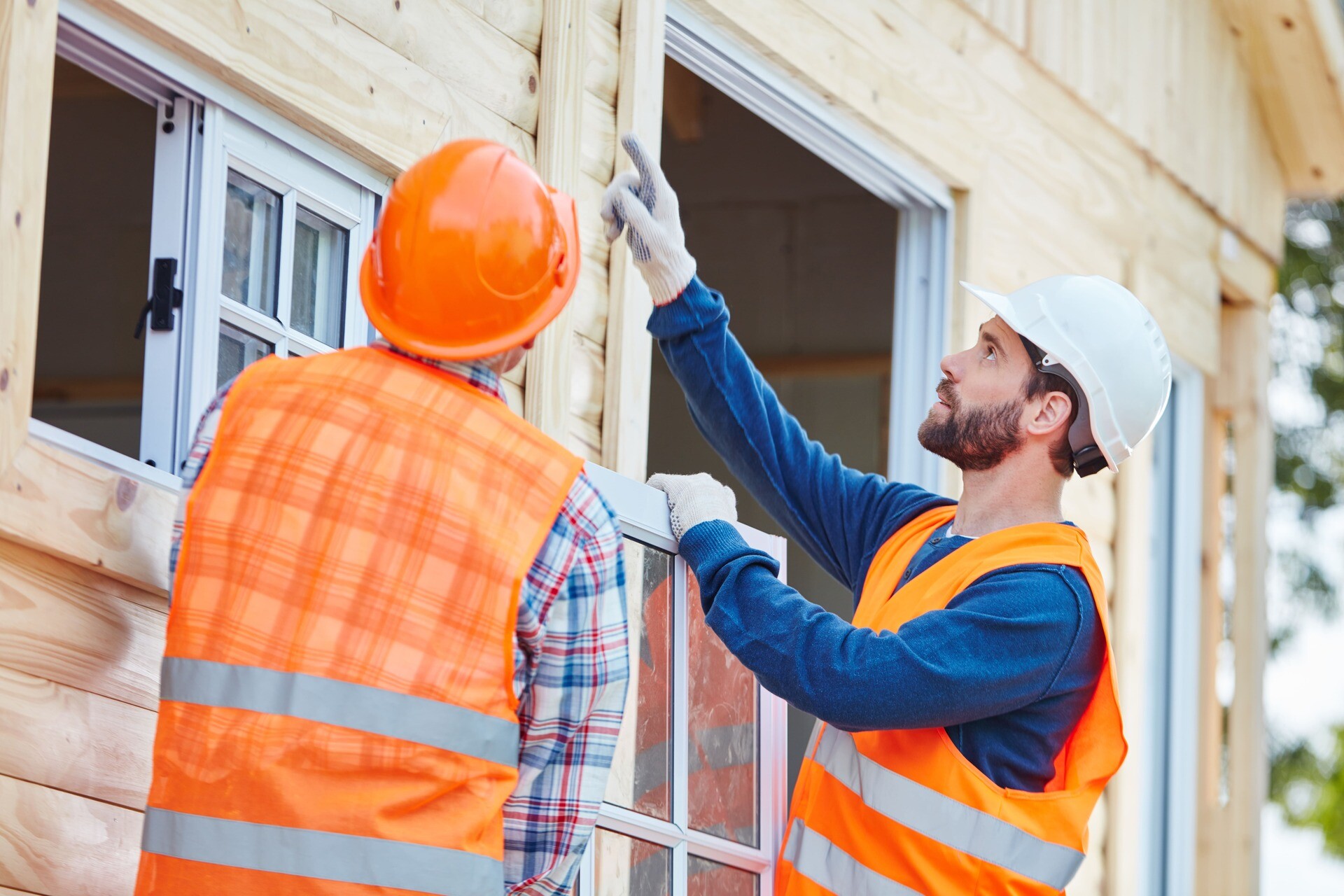 Zwei Bauarbeiter setzen ein Fenster in ein Holzhaus ein.