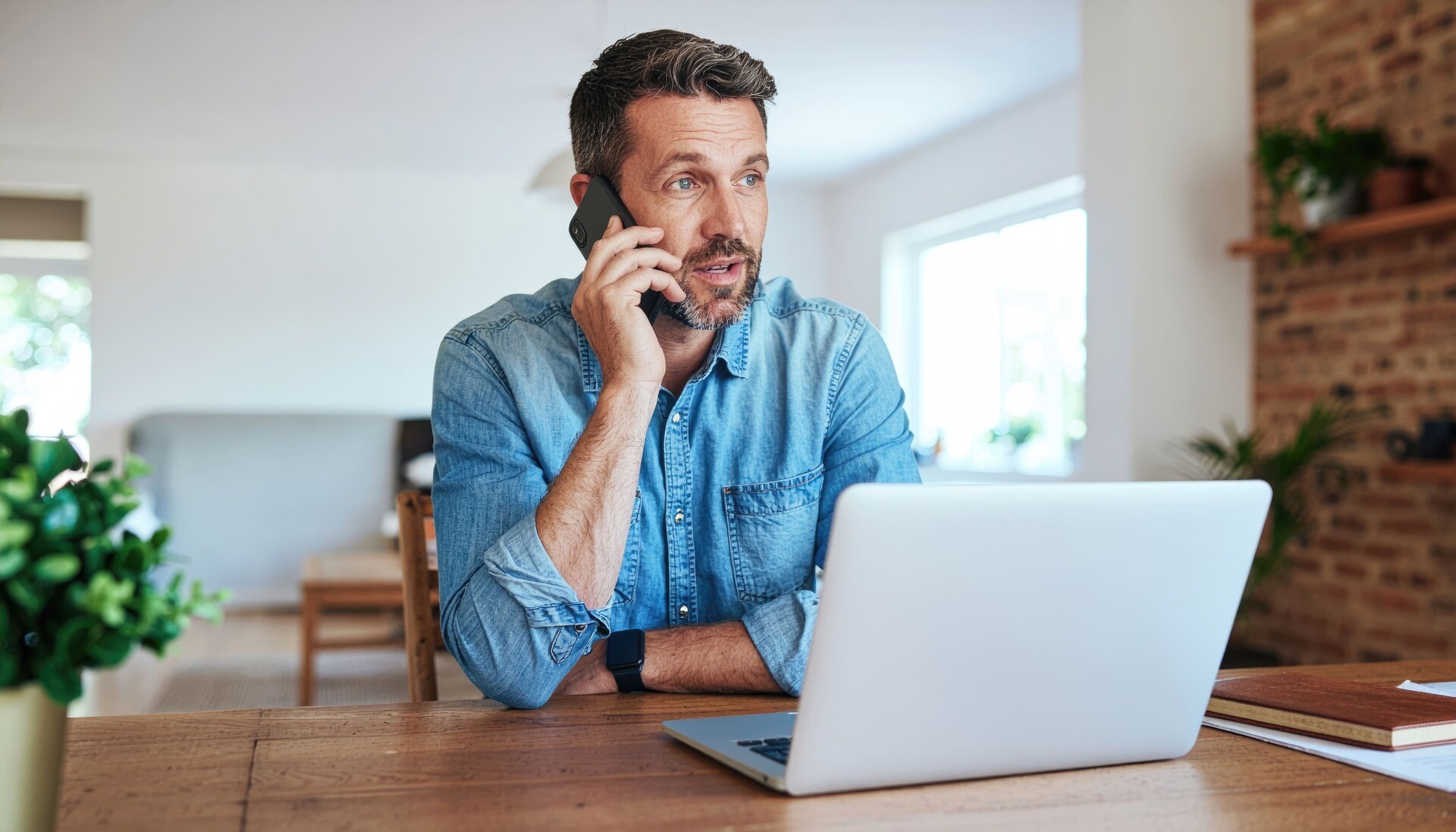 Mann sitzt am Laptop und telefoniert für Immobilienkauf