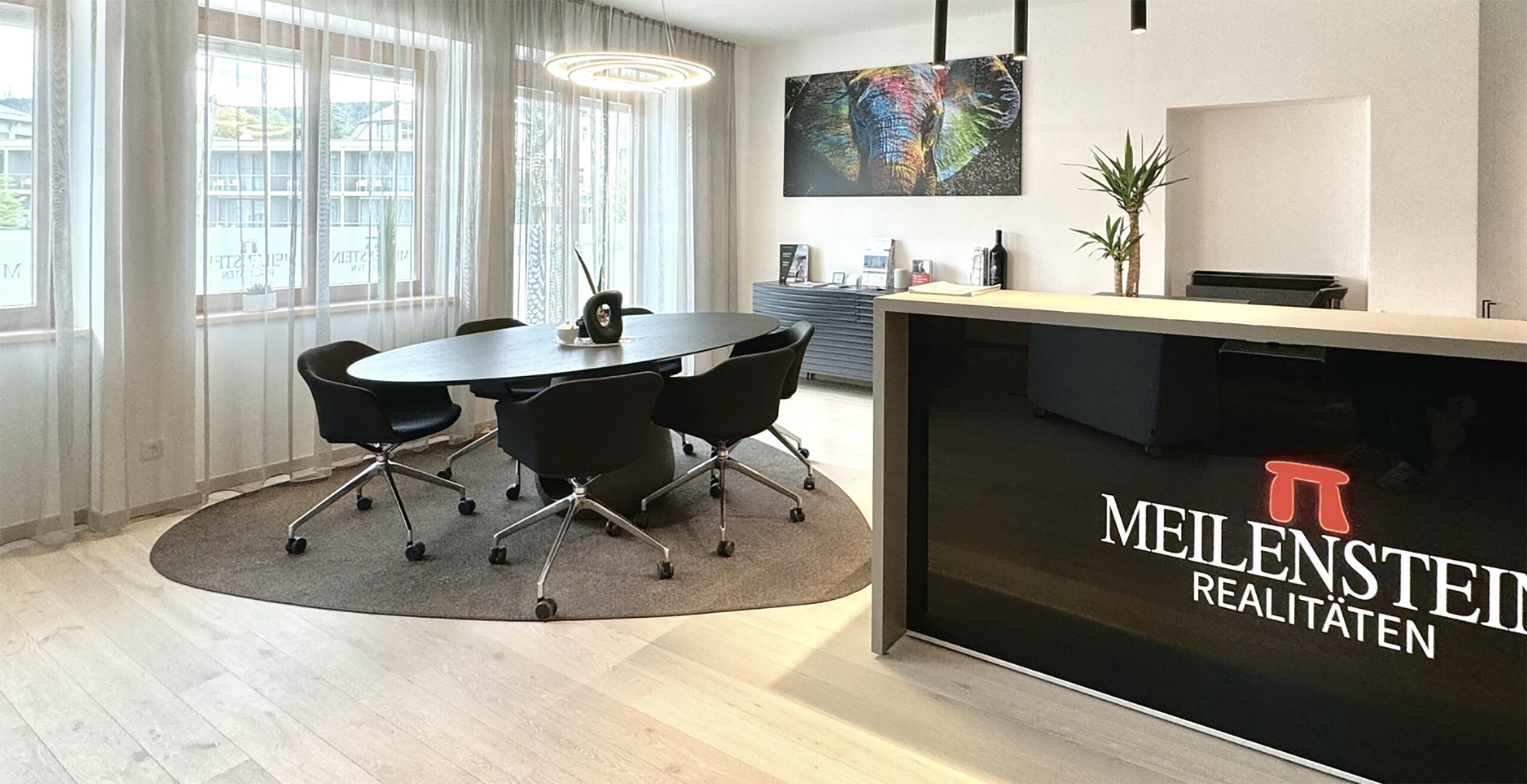 Büro mit rundem Tisch, schwarzen Stühlen, großen Fenstern, Schild.