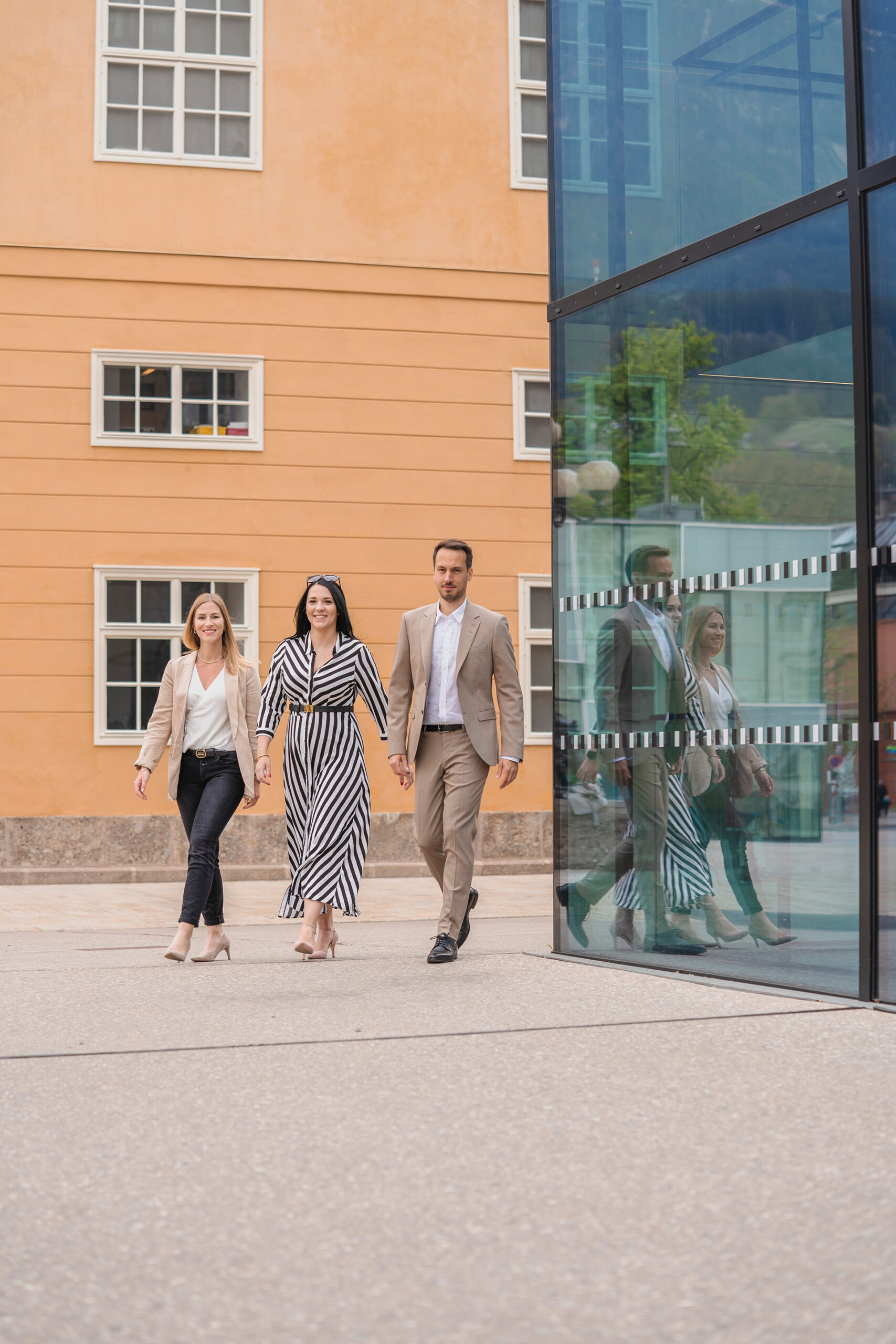 Drei Personen gehen vor einem modernen Gebäude mit Glas und Orange.