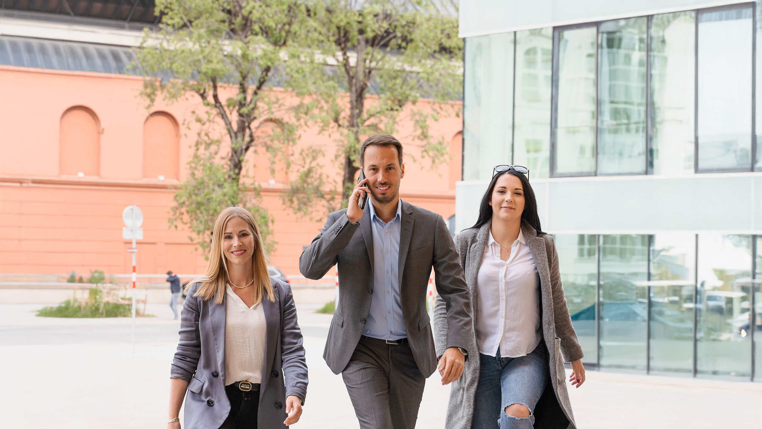 Drei Menschen in Businesskleidung gehen draußen und lächeln.