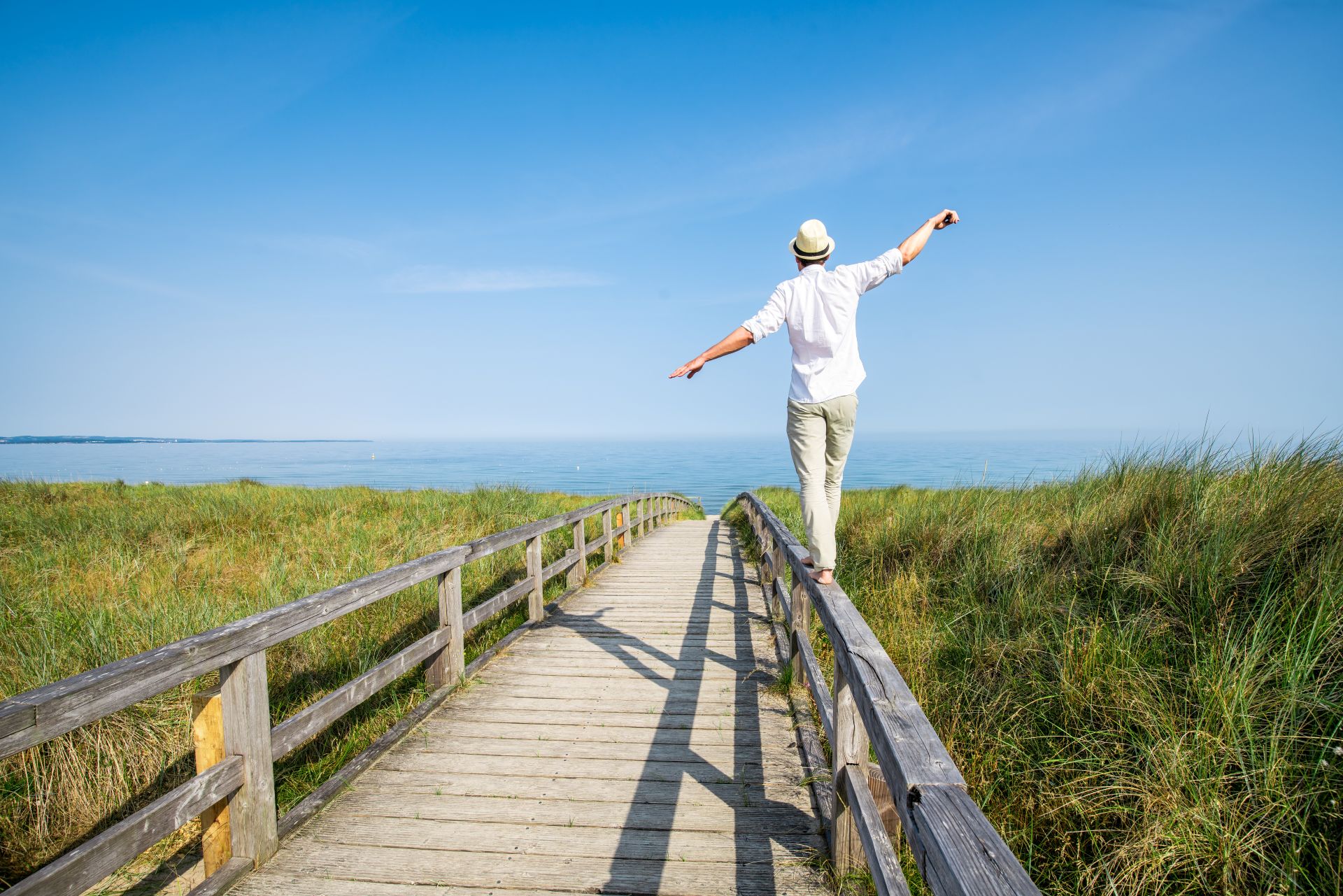 Person auf Steggeländer am Meer, umgeben von Gras und Himmel.