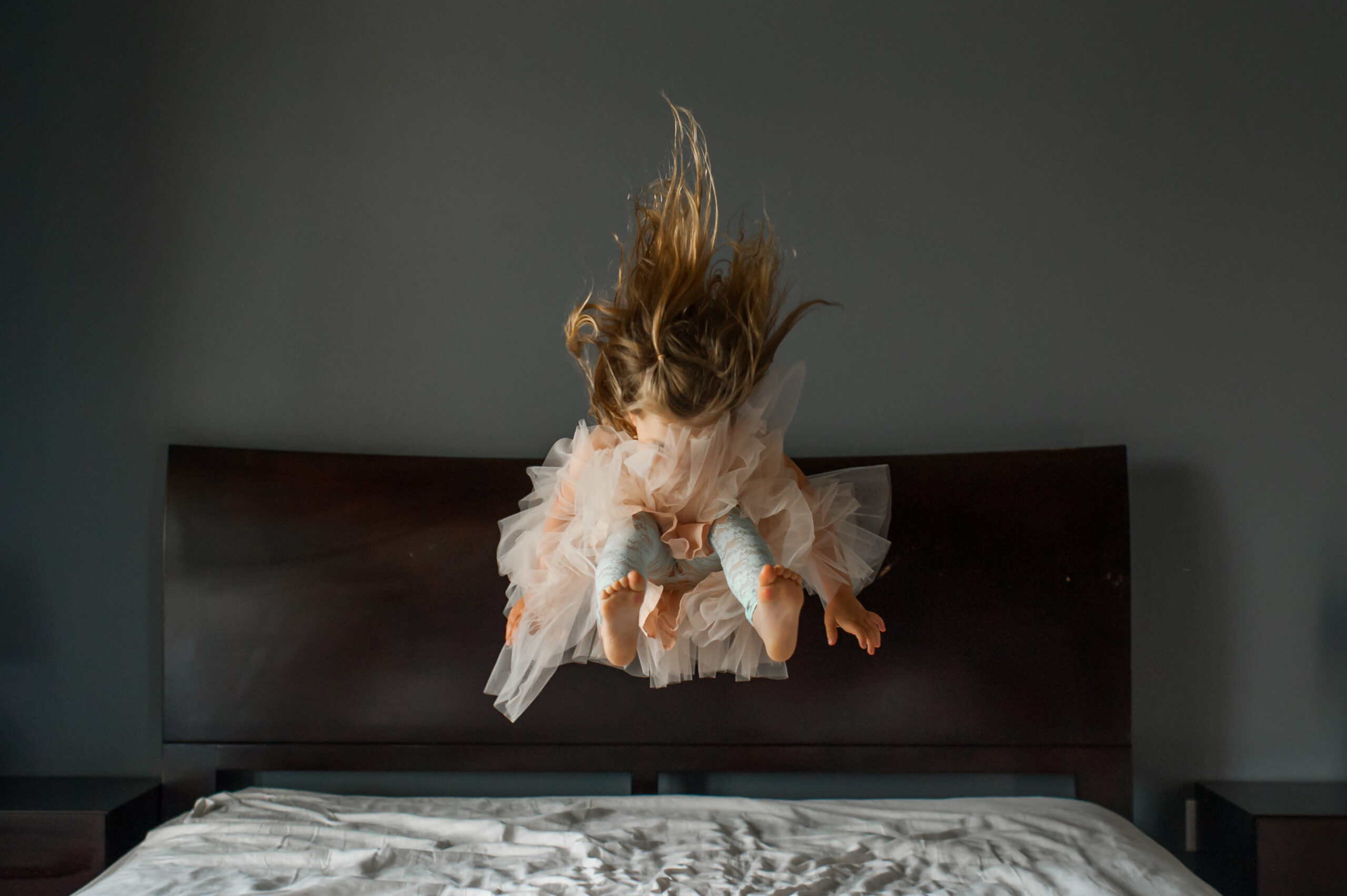 Mädchen im Tutu springt auf dem Bett, Haare fliegen nach oben.