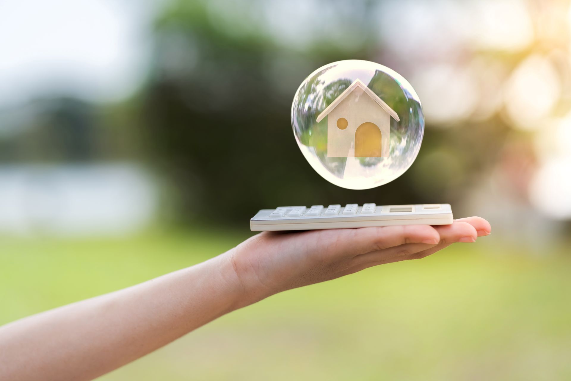Hand mit Rechner, darüber schwebt ein Symbolhaus im Freien.